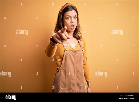 Jeune belle fille blonde portant globalement debout sur fond isolé jaune pointant mécontenté et