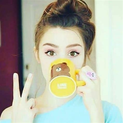 A Woman Holding Up A Cup With A Teddy Bear On It And Making The Peace Sign