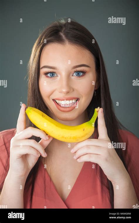 A Pretty Teenage Girl Holding A Banana In Both Hands Close To Her Face