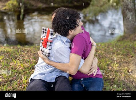 Happy Gay Couple Hugging In A Park After Exchanging Gifts On Their Anniversary Stock Photo Alamy