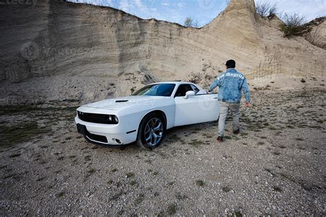 Back of man in jeans jacket and cap open door of his white muscle car