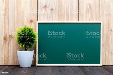 Blank Green Chalkborad With Wood Frame And Little Decorative Tree In White Vase On Wooden Table