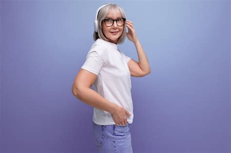 Dame mature aux cheveux gris écoute de la musique dans des écouteurs sans fil sur fond de studio
