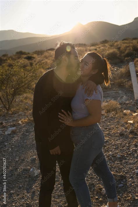 Side View Portrait Of A Amazing Couple Kissing Against Sunset Outside While Traveling In Their