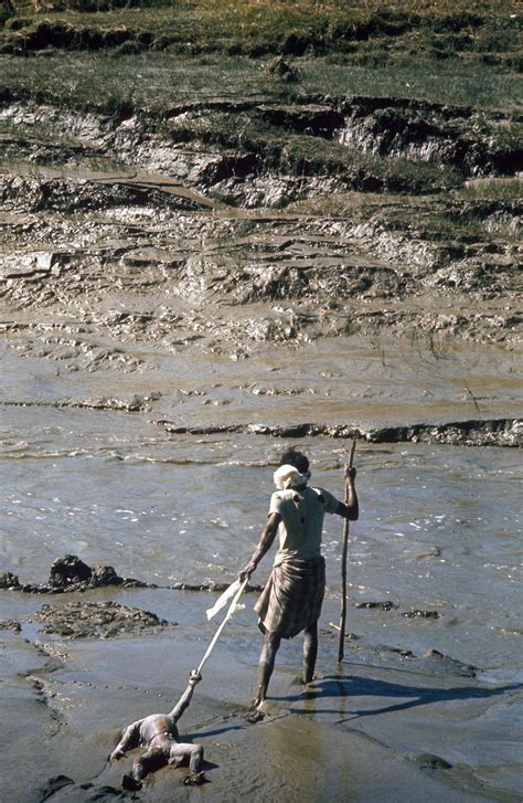 A Worker Drags The Limed Corpse Of A Young Boy Into A River For