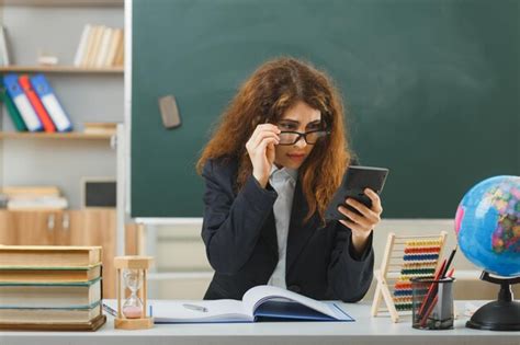 Удивленная молодая учительница в очках держит и смотрит на калькулятор ...