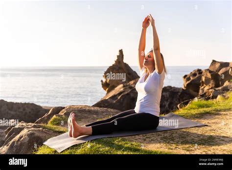 A Blonde Woman Doing Yoga Exercises In Nature By The Sea Stretching Next To A Lighthouse