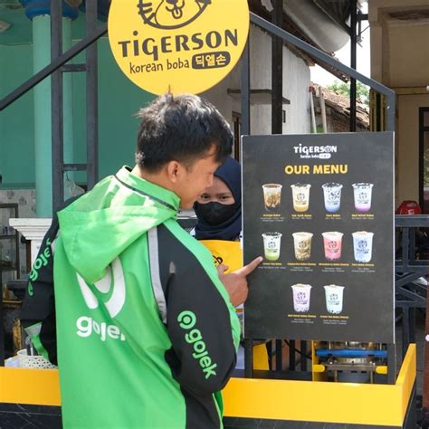 A Man Standing In Front Of A Sign With Drinks On It That Says Tigerson