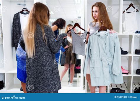 Female Shop Assistant Offering Two Items Of Clothes To The Customers In