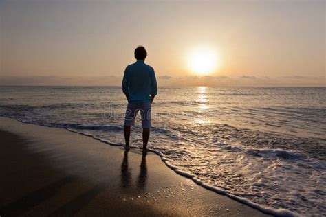 Hombre Solamente En La Playa Que Mira La Puesta Del Sol Foto De Archivo