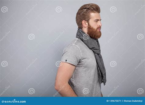 Young Handsome Bearded Man Standing By The Grey Wall Rotated In Profile