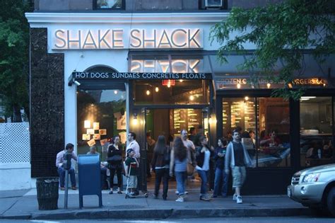 A Group Of People Standing In Front Of A Shake Shack On A City Street