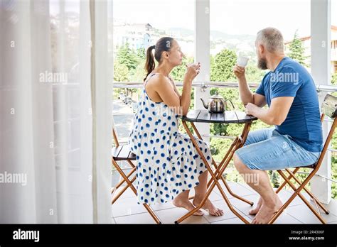 Wife And Husband Drinking Hot Beverage In Mugs Sit On Hotel Balcony Enjoying City View Married