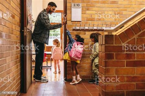 Elementary School Teacher Greeting His Students At The Door Male ...