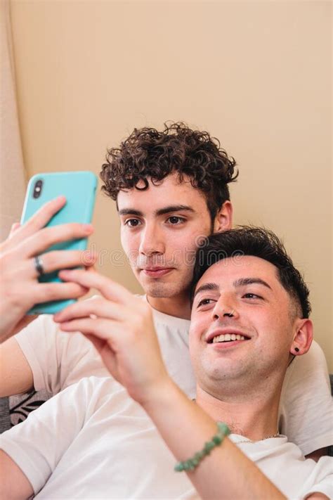Close Up Of A Gay Couple Lying On The Sofa And Using The Mobile To Interact On Social Media