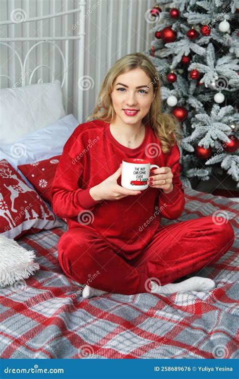 A Beautiful Blonde Girl In Red Pajamas Sits On A Bed With A Cup Of Hot Drink In Her Hands Girl