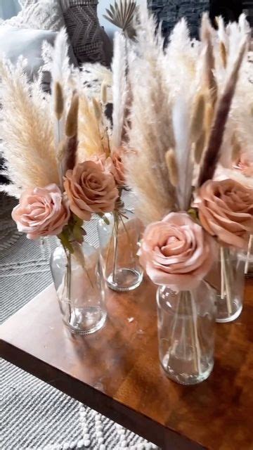 Three Vases Filled With Flowers And Feathers On Top Of A Wooden Table