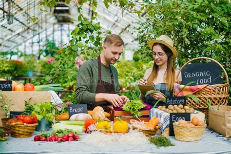 Cheerful Young People Farmers Putting Organic Food On Table At Farm