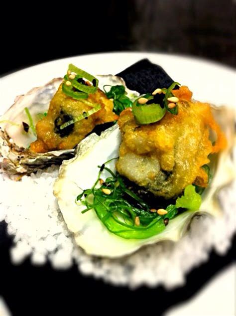 an open oyster shell on a white plate with green garnish and sesame seeds