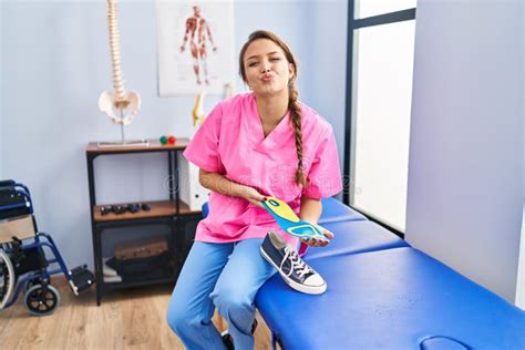 Young Hispanic Woman Holding Shoe Insole at Physiotherapy Clinic Looking at the Camera Blowing a ...