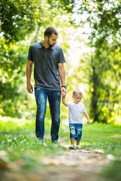 Feliz Joven Padre Sosteniendo A Su Peque O Hijo Con La Mano Y Caminando