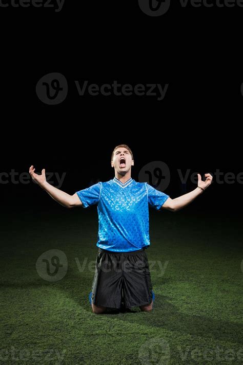 Soccer Player Kneeling On Pitch With Arms Out Stock Photo At