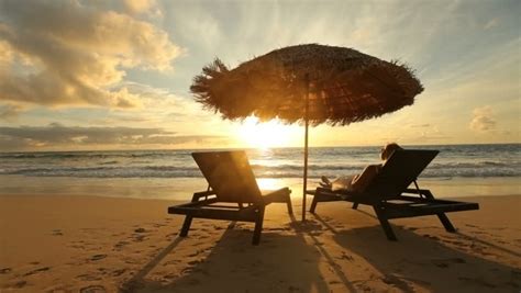 Romantic Couple Sitting In Wooden Deckchairs On The Beach Toasting The