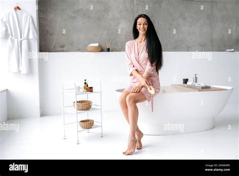 Beautiful Caucasian Brunette Long Haired Woman In A Dressing Gown Sit In A Bathroom On The
