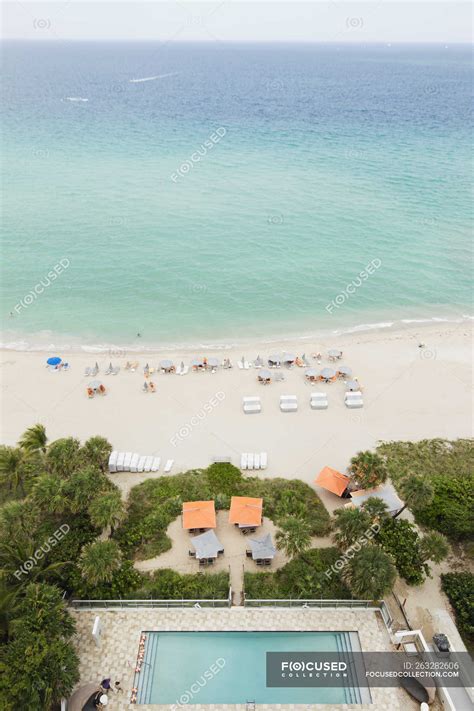 High Angle View Of Hotel Pool And Beach With Chairs And Tourists