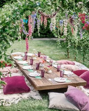 A Picnic Table With Purple And Pink Pillows On It Surrounded By Lush