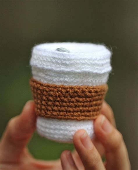 a person holding up a crocheted coffee cup