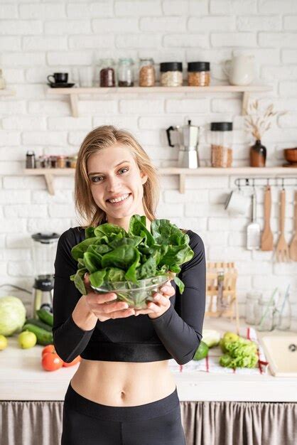 Premium Photo Portrait Of Smiling Young Woman Holding Spinach In Kitchen