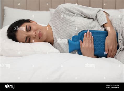 Woman Using Hot Water Bottle To Relieve Menstrual Pain On Bed At Home Stock Photo Alamy