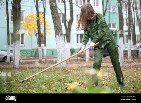 A Girl With A Rake Cleans The Lawn A Woman In Uniform Brings Order A