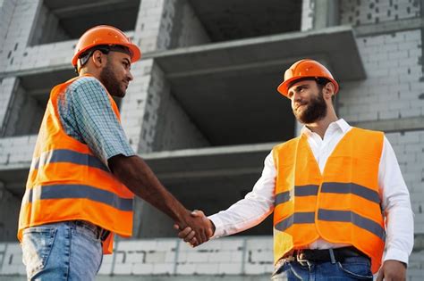 Dos hombres ingenieros en ropa de trabajo un apretón de manos contra el