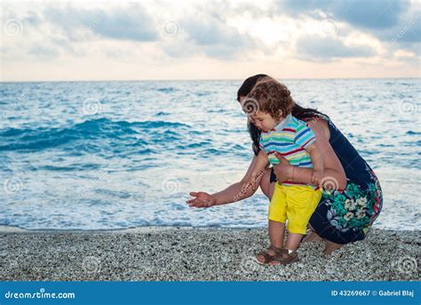 La Madre Y El Ni O Recogen Los Guijarros En La Playa Foto De Archivo