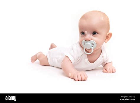 Baby Baby With A Pacifier In His Mouth Lies In Surprise On A White