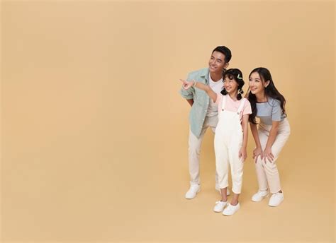 Premium Photo Asian Father And Mother Daughter Hand Pointing Finger Isolated On Nude Color