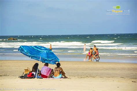 Imagem de três amigas embaixo do guarda sol azul curtindo a paisagem da