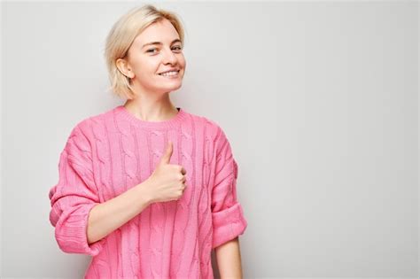 Portrait D Une Jeune Femme Blonde En Pull Rose Souriant Joyeusement Montrant Le Geste Du Pouce
