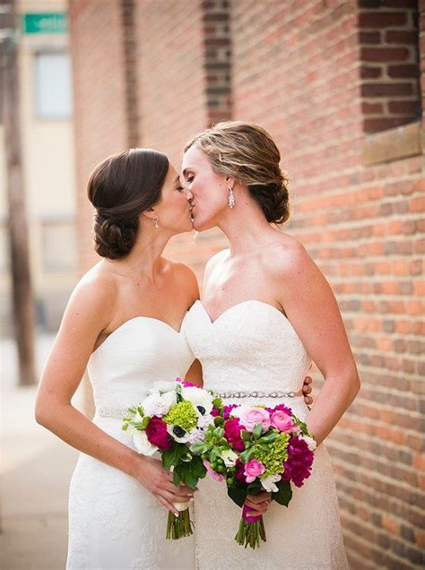 two brides are kissing each other in front of a brick wall and holding ...