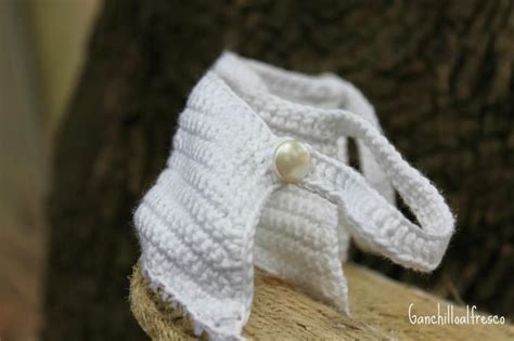 A White Crocheted Shoe With A Pearl Button On The Side And A Tree Trunk