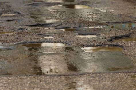 Buracos e poças na estrada de asfalto molhada quebrada ruim após a