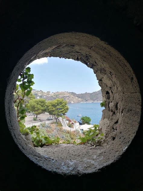 The View Through A Hole In A Rock Wall Looking Out At Water And Hills