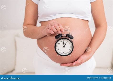 A Pregnant Woman With A Naked Belly Holds An Alarm Clock Intended Date Of Birth Stock Image