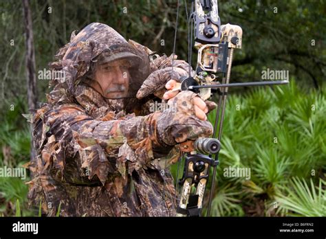 Hunter wearing camouflage outfit with hunting bow kneels in the woods ...