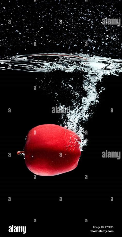 Close Up View Of Red Apple Falling Into Water Isolated On Black Stock