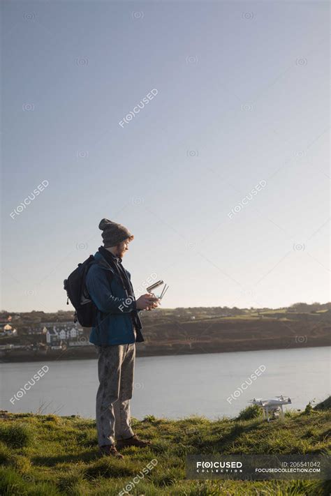 Male hiker operating drone near lake at countryside — woolly hat, gadget - Stock Photo | #206541042