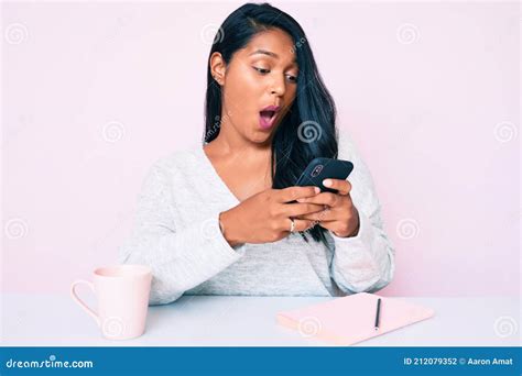 Bella Joven Latina De Pelo Largo Usando Smartphone Sentada En La Mesa Asustada Y Asombrada Con