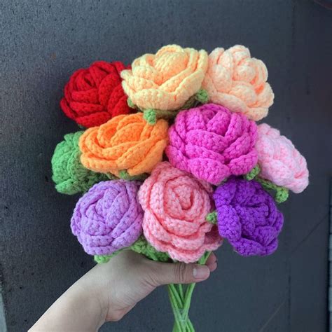 A Hand Holding A Crocheted Bouquet Of Flowers On A Gray Background With